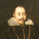 Fragment obrazu olejnego. Przedstawia mężczyznę z wąsami i bródką ubranego w ciemny strój, z białym kołnierzem przy szyi. Na piersiach wisi mu łańcuch. Jest to król Zygmunt III Waza. 