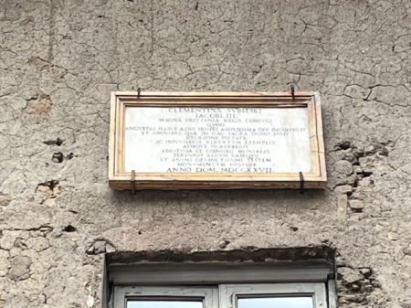 Kamienna tablica pamiatkowa na ścianie szarego budynku.