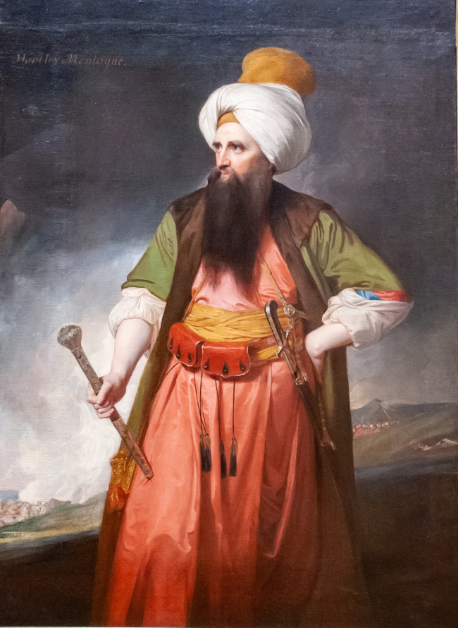 Obraz przedstawia postawnego, brodatego mężczyznę w stroju tureckim, z wysokim turbanem na głowie, szablą u pasa i buławą w prawej dłoni, w tle widoczny krajobraz